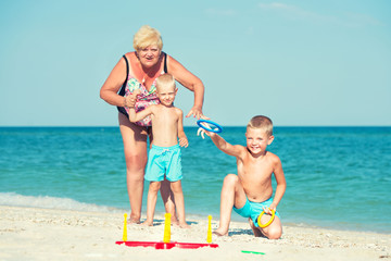 Grandmother with grandchildren playing  a game throwing rings on the beach.