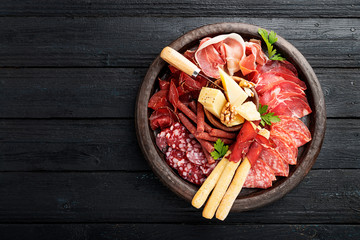 Antipasto platter cold meat with breadsticks, prosciutto, slices ham, beef jerky, salami and cheese platter on wooden board over rustic background. 