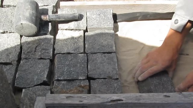 Work on laying natural granite paving stones. A male worker installs granite cobblestones for a sidewalk, yard landscaping, patio or other street design, video without sound