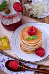 Stack of pancakes decorated with raspberry and mint on a white plate. Village style