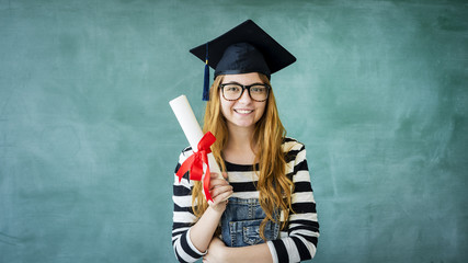 Young student holding diploma on green chalkboard