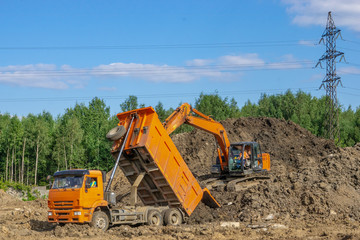 Orange excavator loads the soil in an orange truck