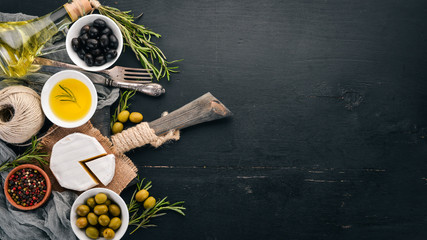 Olives, olive oil, cheese and spices. On a black wooden background. Free space for text.