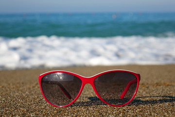 Fototapeta na wymiar Red sunglasses on the sand on the beach, holiday season