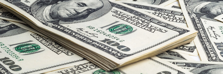 A pack of one hundred dollar bills in the background of scattered dollars. View at an angle, from...