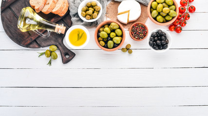 Green olives and black olives, oil, bread, cheese and snacks. Italian cuisine. On a white wooden table. Top view. Free space for text.