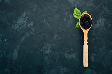 Fototapeta na wymiar Fresh blackberry in a spoon. On a black stone background. Top view. Free space for text.