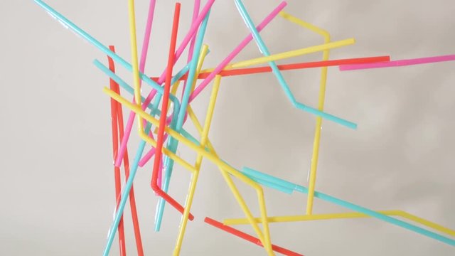 brightly colored plastic single use bendable straws tossed in a clump into water against a neutral white background