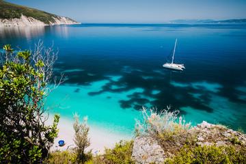 Fteri beach, Cephalonia Kefalonia, Greece. White catamaran yacht in clear blue sea water. Tourists on sandy beach near azure lagoon