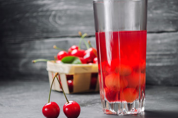juice or compote with cherries. fresh ripe red cherry in a basket on a gray concrete background, summer berry, summer drink