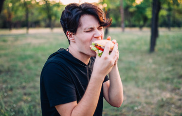  guy eats a burger in the park in summer