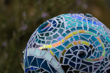 Close-up of mosaic garden ball in multicolored shades of blue made from stained glass tiles, abstract design dipicting the flow of water