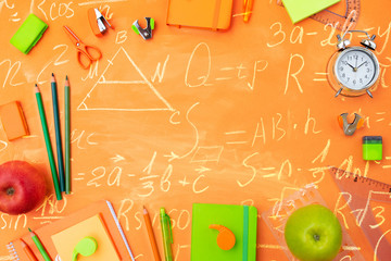 Back to school styled flat lay frame with multicolored school supplies on orange background with math formulas
