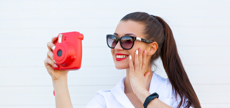 Fashion portrait of pretty smiling woman in sunglasses making photo by the camera against the grey wall. Wireless Headphones, fitness bracelet on the hand