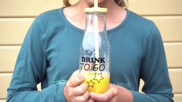 Girl drinking orange juice from a glass bottle with the inscription - Drink to Go