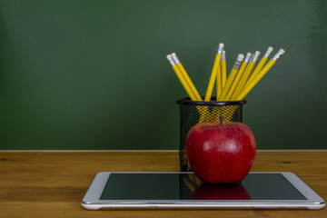 Tableta digital y manzana en el escritorio frente a la pizarra