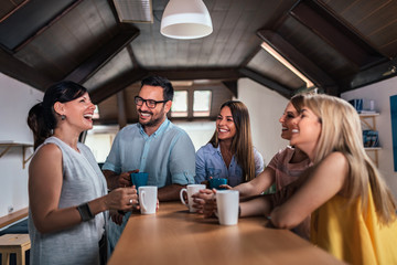 Five friends laughing while drinking tea or coffee at counter table.