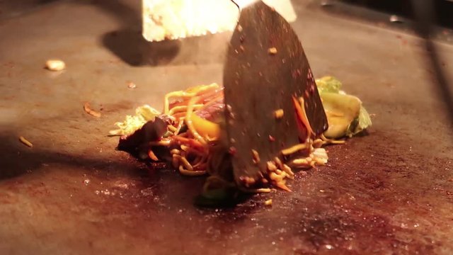 A footage of Chao mein being pan fried on a tepanyaki table. footage is taken in 60 fps and edited in 30 fps. footage is slowed by 50%.