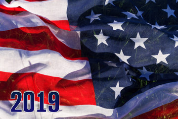 The background of the American flag and 2019. The flag of the USA lies on the green grass, and on it the voluminous figures are 2019.