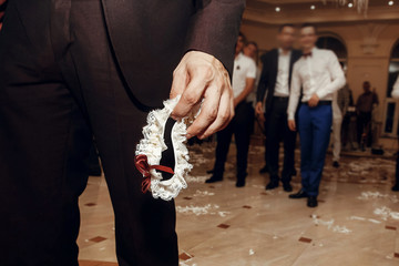groom holding silk garter from bride at wedding party. tradition of throwing bridal garter to man, having fun at  wedding reception in restaurant.