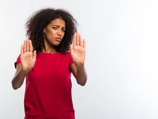 Portrait of serious young african woman in red t-shirt showing stop gesture with her palms isolated over white wall background. Decline concept.