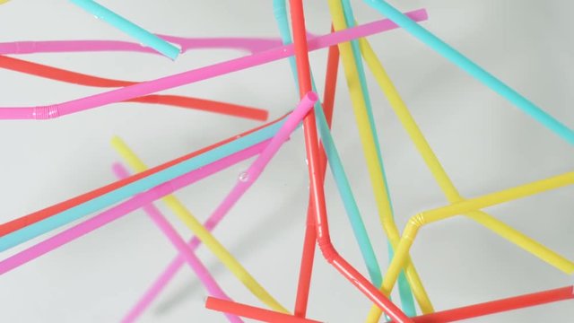 Close on brightly colored plastic single use bendable straws floating on the surface of water against a neutral white background