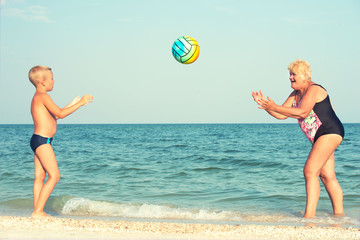Grandmother with grandson on beach playing ball.