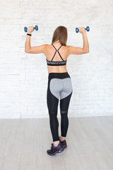 Fototapeta na wymiar Back view of sporty woman with dumbbells. Rear view of sportive woman. Strong woman. Beautiful young sporty muscular fitness model