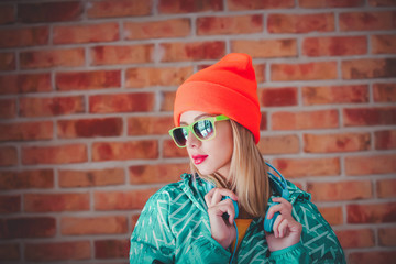 Young blonde girl in 90s sports jacket and hat on brick wall background