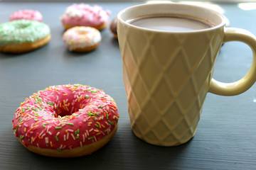 Glass Cup of hot coffee on a black table surrounded by colorful donuts close-up