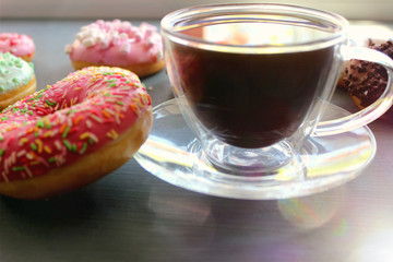 Glass Cup of hot coffee on a black table surrounded by colorful donuts close-up