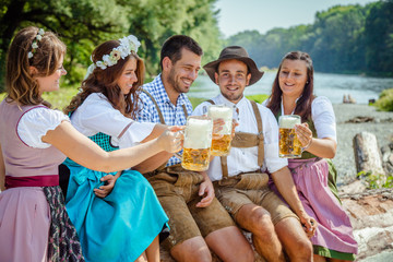 Oktoberfest Freunde in Lederhosen und Dirndl trinken Bier an der Isar