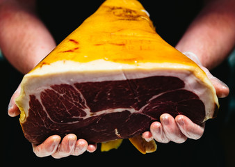 A butcher holds a whole piece of cured meat