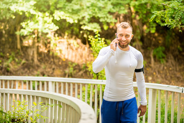 Young man talks on the phone and takes a break from jogging through the countryside