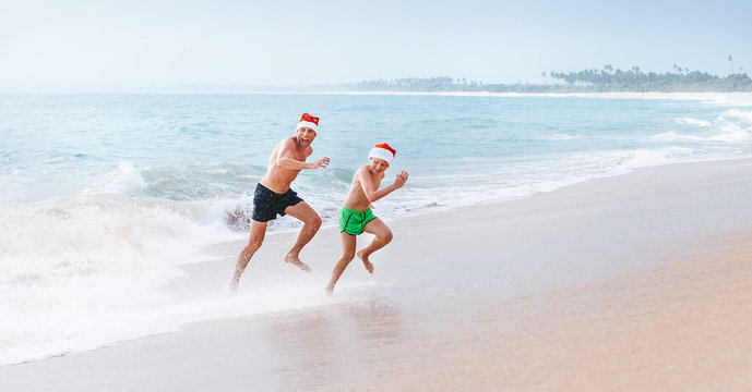 Father and son have a fun on ocean beach, run away from big waves. Christmas holiday time. Tropical vacation