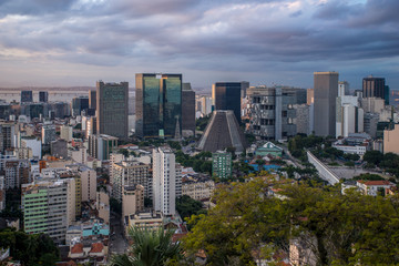 High vantage view of the city centre of Rio de Janeiro with skyscrapers and the cone shaped cathedral in the middle at sunset with dramatic clouds overhead