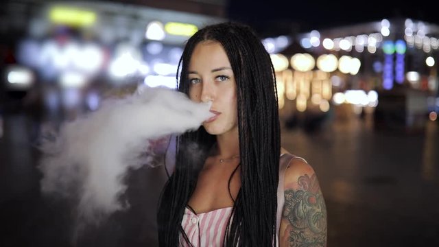 Unconventional woman smoking e-cigarette at the night city