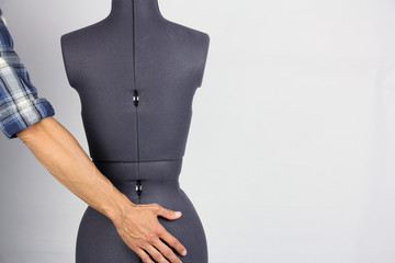 man holds his hand on the ass of female sewing mannequin, rear view, gray background