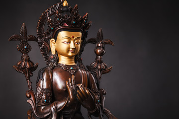 The Buddha of future - Buddha Maytereya`s figure in a dharmachakra mudra pose. The statue brown color made of metal on a dark background.