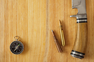 Self-made hunting knife, compass and cartridge for a rifle on a wooden background. Close-up