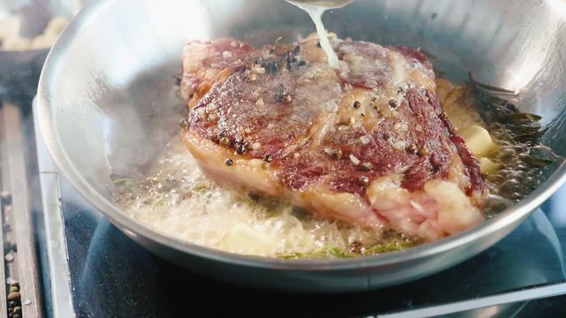 Meat steak is fried in butter and grease on frying pan, close-up in slow motion.