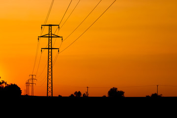 Electricity towers silhouettes on a field during the sunset