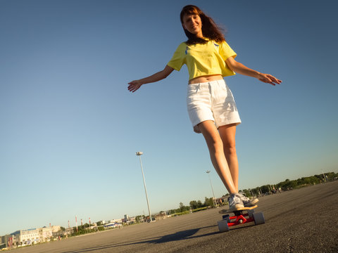 Street Sports: A girl in a bright yellow T-shirt is rolling on a longboard on the city's asphalt.