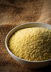 Heap of raw, uncooked couscous in white bowl on burlap