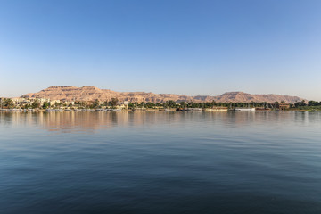 Cityscape from water Nile River with green trees and desert mountain, next to ancient Thebes, in Luxor, Egypt, Africa