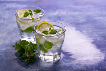 Lemon water, lemonade in two glasses, detox, blue background