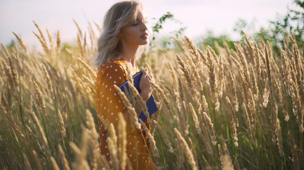 Beautiful happy young woman in field of spikelets and wheat with book on the sunset, blonde in the grass having a good time