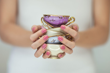 Beautiful woman hands with perfect pink nail polish holding little vintage tea cups, romantic shabby chic mood, can be used as background