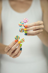 Beautiful woman hands with rainbow nail polish holding colorful swirl lollypops, funny cheerful, can be used as background 
