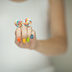 Beautiful woman hands with rainbow nail polish holding colorful swirl lollypops, funny cheerful, can be used as background 